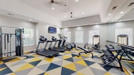 Located at 2801 E 120th Ave in Thornton, Colorado, this fitness center is a well-equipped, single-floor exercise facility designed to support a full range of workout routines. The space is immediately eye-catching thanks to its bold geometric-patterned carpet in yellow, navy, and gray tones, adding a dynamic and energetic ambiance to the room.

The layout is thoughtfully organized into distinct workout zones. The cardio area features multiple treadmills, elliptical machines, and a rowing machine, all positioned near windows fitted with blinds that allow natural light to filter in while maintaining comfort. A wall-mounted flat-screen TV provides entertainment during workouts. The strength training area includes a multi-station cable machine, a dumbbell rack with a variety of free weights, and a weight bench, offering options for both beginners and experienced lifters.

A full-length mirror spans one wall, visually expanding the space and allowing users to monitor their form. Recessed lighting and ceiling fans keep the environment bright and well-ventilated. The elevated tray ceiling adds to the sense of openness and height throughout the room. Sanitation stations with paper towel dispensers and hand sanitizer are conveniently placed, and a dedicated nook near the cable machine provides easy access to resistance bands and accessories. French doors offer a welcoming entry point into this clean, functional, and motivating fitness environment.