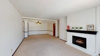 This single-floor residence offers a practical and comfortable layout designed for easy living. The expansive living area is the centerpiece of the home, featuring plush neutral carpeting, a striking white brick fireplace with a dark mantel, and an open flow into the dining area, which is equipped with a ceiling fan and exposed ceiling beams. Large vertical blinds and windows allow natural light to fill the space throughout the day.

The kitchen is efficiently designed with warm wood cabinetry, light countertops, a double basin sink, and black appliances including a range and dishwasher. A stacked washer and dryer unit is conveniently integrated within the kitchen area, adding everyday functionality.

The bedrooms are generously sized, each finished with soft carpeting, baseboard heating, and windows with blinds that provide natural light and privacy. The rooms offer ample wall space and a clean, neutral palette suitable for a variety of uses.

Two full bathrooms serve the residence. One features a tub-shower combination with a curtain, tile flooring, and a warm wood vanity with light countertops. The second bathroom offers a similar vanity setup and includes a separate tub area. Both bathrooms are finished with tile flooring and provide functional, well-organized layouts. Overall, the home presents a clean and move-in ready environment.