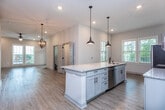 This two-story residence in Charleston, South Carolina, showcases a thoughtfully designed interior with a blend of modern finishes and functional layouts across both levels. The open-concept kitchen serves as a focal point, featuring an elongated granite-topped island with an undermount sink, pendant lighting with an industrial aesthetic, and white shaker cabinetry that extends to the ceiling for generous storage. Stainless steel appliances, including a French door refrigerator, range, and microwave, complement a classic subway tile backsplash. Light wood-style flooring flows throughout the main living areas, enhancing the bright, neutral palette.

The living areas are spacious and well-lit, with recessed lighting, ceiling fans, and multiple windows inviting natural light. A chandelier adds a refined touch near the stairwell. Upstairs, bedrooms feature vaulted ceilings, plush carpeting, and oversized windows offering views of the surrounding neighborhood. The primary bedroom connects directly to a bathroom, while additional bathrooms include dual-sink vanities with granite countertops, wood-toned cabinetry, and tub-shower combinations with subway tile surrounds and matte black fixtures throughout.