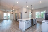 This two-story residence in Charleston, South Carolina, showcases a thoughtfully designed interior with a blend of modern finishes and functional layouts across both levels. The open-concept kitchen serves as a focal point, featuring an elongated granite-topped island with an undermount sink, pendant lighting with an industrial aesthetic, and white shaker cabinetry that extends to the ceiling for generous storage. Stainless steel appliances, including a French door refrigerator, range, and microwave, complement a classic subway tile backsplash. Light wood-style flooring flows throughout the main living areas, enhancing the bright, neutral palette.

The living areas are spacious and well-lit, with recessed lighting, ceiling fans, and multiple windows inviting natural light. A chandelier adds a refined touch near the stairwell. Upstairs, bedrooms feature vaulted ceilings, plush carpeting, and oversized windows offering views of the surrounding neighborhood. The primary bedroom connects directly to a bathroom, while additional bathrooms include dual-sink vanities with granite countertops, wood-toned cabinetry, and tub-shower combinations with subway tile surrounds and matte black fixtures throughout.