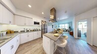 Located at 1480 E Paseo Verde Pkwy in Henderson, NV, this well-appointed one-bedroom, one-bathroom residence offers a thoughtfully designed open-concept layout. The kitchen is a standout feature, boasting crisp white shaker cabinetry, dark countertops, a full suite of stainless steel appliances including a gas cooktop with a bold overhead range hood, built-in microwave, dishwasher, and refrigerator, plus a convenient wine rack. A central island with bar seating flows naturally into the combined dining and living area, where wood-style flooring, large windows, and abundant natural light create a welcoming atmosphere. The living room offers generous wall space and views of palm trees through bright, curtained windows. The bedroom features plush carpeting, a ceiling fan, a sliding barn-door closet, and direct access to a private balcony with outdoor views. Two closets provide ample storage. The bathroom includes a soaking tub and shower combo, a single vanity with a stone-tone countertop, and wood-style flooring. A dedicated laundry area and a private balcony complete this comfortable and functional Henderson residence.