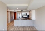 Located at 2610 109 Street NW in Edmonton, Alberta, this thoughtfully designed one-bedroom, one-bathroom unit offers a clean, modern aesthetic throughout its efficiently organized single-floor layout. Light-toned luxury vinyl plank flooring runs continuously through the space, complementing the neutral warm beige and white walls that create a bright, welcoming atmosphere.

The open-concept kitchen serves as a central feature, showcasing a large island with a double stainless steel sink and dark quartz countertops, two-tone cabinetry in white and natural wood finishes, a herringbone tile backsplash, and a full suite of stainless steel appliances including a French door refrigerator, electric range, and over-the-range microwave. A built-in wine rack adds a refined touch. The kitchen flows seamlessly into the living area, which is bathed in natural light through expansive floor-to-ceiling windows offering sweeping views of the surrounding Edmonton landscape.

The bedroom is a comfortable and well-proportioned retreat, featuring large windows with the same open views, a sliding-door closet, and warm overhead lighting. Additional storage is provided by a second closet accessible from the hallway. The bathroom includes a full soaker tub and shower combination with chrome fixtures. In-suite laundry adds further convenience to this well-appointed urban residence.