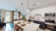 Located at The Ballast on Salem in Apex, NC, this well-appointed one-bedroom, one-bathroom residence offers a smart and stylish single-floor layout. The open-concept kitchen and dining area is a true centerpiece, featuring two-tone cabinetry with crisp white upper cabinets and dark lower cabinets, quartz countertops, a subway tile backsplash, stainless steel appliances, and a large island with seating — ideal for both cooking and entertaining. The living room flows seamlessly from the kitchen, bathed in natural light through large windows and a glass door that opens to a private balcony with outdoor views. Light wood-style flooring runs throughout the main living areas, complementing the bright, airy aesthetic. The bedroom offers a comfortable and cozy retreat with plush carpet, a ceiling fan, natural light, and a well-organized closet with built-in shelving. The bathroom is outfitted with a dual-sink vanity, dark cabinetry, quartz countertops, and a large framed mirror. Additional conveniences include a dedicated entrance with a built-in nook, a pantry, laundry, and hallway storage, making efficient use of every square foot in this thoughtfully designed residence.