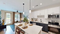 Located at The Ballast on Salem in Apex, NC, this well-appointed one-bedroom, one-bathroom residence offers a smart and stylish single-floor layout. The open-concept kitchen and dining area is a true centerpiece, featuring two-tone cabinetry with crisp white upper cabinets and dark lower cabinets, quartz countertops, a subway tile backsplash, stainless steel appliances, and a large island with seating — ideal for both cooking and entertaining. The living room flows seamlessly from the kitchen, bathed in natural light through large windows and a glass door that opens to a private balcony with outdoor views. Light wood-style flooring runs throughout the main living areas, complementing the bright, airy aesthetic. The bedroom offers a comfortable and cozy retreat with plush carpet, a ceiling fan, natural light, and a well-organized closet with built-in shelving. The bathroom is outfitted with a dual-sink vanity, dark cabinetry, quartz countertops, and a large framed mirror. Additional conveniences include a dedicated entrance with a built-in nook, a pantry, laundry, and hallway storage, making efficient use of every square foot in this thoughtfully designed residence.
