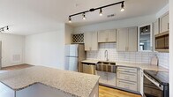 Located at 9051 Seneca Dr in Wilmington, NC, this thoughtfully designed one-bedroom, one-bathroom residence offers a comfortable and functional single-floor layout. The open-concept kitchen and living area serves as the heart of the home, showcasing shaker-style cabinetry in a soft gray-white finish, granite countertops, a classic white subway tile backsplash, and a full suite of stainless steel appliances including a refrigerator, dishwasher, microwave, and range. A central island with additional granite counter space provides extra prep room and casual seating. Track lighting illuminates both the kitchen and living area, which features warm hardwood-style flooring and direct access to a private balcony with outdoor views. The bedroom is a well-sized retreat finished with plush carpet, a ceiling fan, and windows that invite natural light. The bathroom is equipped with a sleek sliding glass shower enclosure and gray cabinetry for storage. A dedicated laundry room houses a full-size washer and dryer. Clean white walls and consistent finishes throughout contribute to a bright, cohesive, and move-in-ready atmosphere.