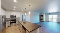 Located at 2065 S Cherokee St in Denver, CO, this two-bedroom, two-bathroom residence offers a well-designed single-level layout with modern finishes throughout. The open-concept living and kitchen area serves as the heart of the unit, anchored by light wood-style flooring and recessed lighting that maintain a clean, contemporary aesthetic. A sliding glass door connects the living space to an outdoor area, allowing natural light to fill the room.

The kitchen is thoughtfully appointed with white shaker-style upper cabinetry, two-tone lower cabinetry, and rich wood-toned countertops. A central island with an undermount sink and pendant lighting provides additional workspace and casual dining potential. Stainless steel appliances, including a refrigerator, range, and microwave, complement the tile backsplash for a cohesive, modern look. A stacked washer and dryer unit is conveniently integrated within the living area.

Both bedrooms feature plush carpeting, ceiling light fixtures, and windows that offer views of the surrounding Denver neighborhood. The neutral color palette throughout creates a bright and versatile living environment suited to a variety of styles.