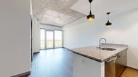 This thoughtfully designed one-bedroom, one-bathroom residence offers a contemporary urban living experience across a single floor. The open-concept living and kitchen area immediately impresses with its striking exposed concrete ceiling, which adds an industrial-chic character balanced by crisp white walls and smooth hardwood-style flooring. Floor-to-ceiling glass doors flood the living room with natural light and open to a balcony with expansive panoramic views of the surrounding cityscape and greenery.

The kitchen is outfitted with granite countertops, a peninsula with an undermount sink, stainless steel appliances including a refrigerator, dishwasher, and range, and contemporary pendant lighting—combining both style and functionality. White cabinetry provides ample storage throughout.

The bedroom is a comfortable, well-proportioned retreat featuring plush carpet flooring, a wall-mounted split HVAC unit, an exposed concrete ceiling detail, and a window framing bright outdoor views. A dedicated closet and an in-unit laundry area with a stacked washer and dryer add practical convenience.

The bathroom is clean and modern, featuring a walk-in shower, granite-topped vanity, and wood-style flooring. Throughout the unit, the design balances industrial elements with refined finishes, creating a cohesive and inviting atmosphere.