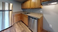 This single-floor, one-bedroom unit offers a well-organized layout designed for comfortable everyday living. The flooring throughout is a standout feature, with rich, dark-toned vinyl plank in the bedroom and living areas, transitioning to lighter wood-look planks in the kitchen — both durable and visually appealing against the cool gray walls.

The living area is generously sized, bathed in natural light from large windows, and includes a wall-mounted AC unit and baseboard heating for year-round comfort. A sliding glass door adds additional natural light and outdoor access. The space flows naturally toward the kitchen, which is well-appointed with warm honey-toned cabinetry, granite-look countertops, a stainless steel dishwasher, refrigerator, and ample upper and lower cabinet storage.

The bedroom is a comfortable, quiet retreat featuring dual windows that invite natural light, a walk-in closet, and continued baseboard heating. The full bathroom includes a clean, white soaking tub and shower combination surrounded by neutral large-format wall tiles, complemented by coordinating floor tile and a toilet.

Overall, the unit presents a clean, updated aesthetic with practical features throughout.