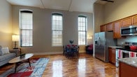This two-story unit blends historic architectural character with modern conveniences. The main level opens to a dramatic living and dining area defined by soaring ceilings, richly toned original hardwood floors, and striking tall arched windows that draw in abundant natural light. The open layout connects seamlessly to a well-appointed kitchen featuring warm wood cabinetry, granite countertops, stainless steel appliances, and ample storage. A cozy seating area completes the main floor's versatile living space.

The upper loft level offers a flexible, carpeted area ideal as a lounge, home office, or additional sleeping space, with angled ceilings that add architectural interest. The private bedroom is tucked away and features rich hardwood flooring, angled ceiling details, and a quiet, restful atmosphere.

The full bathroom is thoughtfully designed with a rich wood vanity, granite countertop, tile flooring, and a convenient stacked in-unit washer and dryer. Throughout both floors, neutral tones create a cohesive, inviting ambiance that balances the unit's historic industrial character with comfortable, contemporary living.