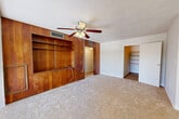 Located at 711 S Lincoln Ave in Clearwater, Florida, this two-bedroom, one-bathroom single-story home offers a practical and comfortable layout. The living area is a standout space, anchored by a full-wall warm wood built-in shelving unit that adds character and retro charm, complemented by a ceiling fan with light fixture and soft carpeted flooring. Windows allow natural light to filter in, brightening the space throughout the day.

The galley-style kitchen is well-appointed with white cabinetry, brushed nickel hardware, neutral countertops, and wood-look flooring. It features a full suite of appliances including a cooktop, refrigerator, and dishwasher, with ample upper and lower cabinet storage on both sides.

The primary bedroom is a generously sized retreat with carpet flooring, a ceiling fan, natural light from a window, and access to a dedicated walk-in closet outfitted with built-in shelving for organized storage. The second bedroom also features carpet, a window with outdoor views, and a well-lit, clean aesthetic.

The bathroom is finished with tile surround, a tub-shower combination, wood-look flooring, a wall-mounted mirror, and a vanity sink. A hallway connects the main living areas, completing this efficiently designed home.