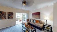 This single-floor residence offers a thoughtfully designed layout that balances comfort and functionality. The living room serves as the heart of the home, featuring wood-look flooring, crown molding, a ceiling fan with light fixture, and a large sliding glass door that opens to an outdoor patio, filling the space with abundant natural light and views of surrounding greenery. A bold abstract canvas anchors the main wall, complementing the inviting sectional sofa and glass-top coffee table.

The kitchen is efficiently laid out with white cabinetry, granite-style countertops, stainless steel appliances including a refrigerator, electric range, microwave, and dishwasher, and a breakfast bar with seating. A dedicated laundry area is conveniently accessible directly from the kitchen.

The residence includes multiple bedrooms, each outfitted with ceiling fans, wood-look flooring, and windows that invite natural light. The primary bedroom features direct access to an en-suite bathroom, while additional bedrooms offer generous closet space and neutral tones conducive to restful living.

The bathrooms are finished in a clean, contemporary style with white vanity cabinetry, broad mirrors, and tile flooring. The primary bath includes a walk-in shower and a walk-in closet. Overall, the space presents a warm and cohesive aesthetic throughout.