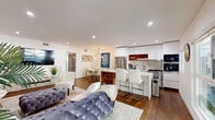 Located in the heart of West Hollywood, this stylish single-story residence at 1267 N Laurel Ave offers a thoughtfully designed open-concept floor plan that seamlessly connects the living, dining, and kitchen areas. Rich hardwood flooring flows throughout, anchoring each space with warmth and continuity.

The living area is bright and inviting, with large windows that invite natural light and offer views of the surrounding neighborhood. The kitchen is a standout feature, showcasing high-gloss white cabinetry, a dramatic marble-veined backsplash, quartz countertops, stainless steel appliances, a built-in oven, and a breakfast bar with white upholstered seating — ideal for both casual dining and entertaining.

The primary bedroom is a serene retreat, featuring recessed lighting, mirrored closet doors, and an en suite bathroom clad in full marble tile. The spa-like bath includes a glass-enclosed walk-in shower, a floating vanity with a teak shelf, and refined chrome fixtures. A second bedroom benefits from generous natural light through large windows, while a second bathroom also features marble tile and a glass shower enclosure.

Throughout the residence, clean white walls, recessed lighting, and contemporary finishes create a cohesive, modern aesthetic that is both functional and refined.