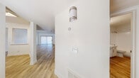 This single-story home showcases a cohesive design built around white-painted brick accent walls and light wood-look flooring that run consistently throughout, creating a bright, clean aesthetic. A hallway with a wall-mounted sconce and multi-switch panel leads to the main living area, which is generously proportioned with vaulted ceilings, a ceiling fan, and a fireplace flanked by a sliding glass door with vertical blinds that invite natural light. The white brick walls add texture and character to the living space without overwhelming the neutral palette.

The kitchen features white shaker-style cabinetry with black hardware, a white countertop, stainless steel appliances including a refrigerator and dishwasher, a black undermount sink, and a window with blinds. The bedrooms continue the white brick wall detailing and wood-look flooring, each equipped with ceiling fans and windows for natural light.

The bathrooms are finished with white cabinetry, white countertops, black hardware, and wood-look tile flooring. One bathroom includes a tub-shower combination, while another offers an elongated vanity. A dedicated laundry room houses a full-size washer and dryer with overhead shelving.