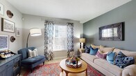 Located at 4515 Desantis Ct in Columbus, Ohio, this thoughtfully designed single-floor residence offers a cohesive blend of comfort and style throughout its well-planned layout. The living room serves as the heart of the home, featuring light hardwood-style flooring, neutral gray walls accented by a deeper slate tone, and a bright window dressed with bold patterned drapes. A curated gallery wall with framed artwork and decorative accents lends the space a warm, eclectic character. The kitchen is outfitted with rich dark cabinetry extending to the ceiling, a tile mosaic backsplash, granite-style countertops, and black appliances, offering both functionality and visual contrast. Two well-sized bedrooms feature plush carpeting, large windows that invite natural light, and accent walls in deep blue-gray tones that create a restful ambiance. A dedicated office space with carpeted floors and a window overlooking the exterior provides a productive and private work environment. The primary bathroom includes a glass-enclosed walk-in shower, dark vanity cabinetry with a granite-topped sink, built-in shelving, and light wood-style flooring. A second bathroom mirrors the refined finishes with a matching vanity and large mirror. This residence offers a polished, move-in-ready environment with consistent design details throughout.