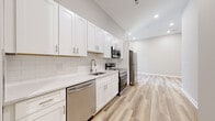 This thoughtfully renovated single-floor unit showcases a bright, contemporary design with light hardwood flooring and neutral tones carried consistently throughout every room. The kitchen is a standout feature, equipped with crisp white shaker cabinetry, brushed nickel hardware, quartz countertops, a classic subway tile backsplash, and a full suite of stainless steel appliances including a refrigerator, electric range, built-in microwave, and dishwasher. Recessed lighting illuminates the space cleanly from above, enhancing the open, airy feel that extends into the adjacent living area, where a window allows in natural light. The hallway connects the spaces efficiently, featuring recessed lighting, louvered closet doors, and a discreetly integrated electrical panel. The bathroom is elegantly appointed with floor-to-ceiling marble-style tile, a soaking tub with shower combination, a white vanity, and polished chrome fixtures, creating a spa-like atmosphere. A dedicated laundry closet with a stacked washer and dryer unit adds everyday convenience. The bedroom offers a clean, open canvas with generous wall space and natural light. Overall, the unit presents a move-in ready, modern living environment with quality finishes throughout.