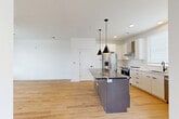 Located at 411 Charles Ave in Charlotte's 28205 zip code, this modern three-story home offers two bedrooms and four bathrooms across a thoughtfully designed layout. The ground floor houses a garage with utility access, a water heater, and an electrical panel. The main living level features an open-concept kitchen and living area bathed in natural light from large, blinds-fitted windows. The kitchen is appointed with white flat-front cabinetry, quartz countertops, stainless steel appliances including a French door refrigerator and range, a wall-mounted range hood, subway tile backsplash, and a substantial dark-toned island with pendant lighting above. Light hardwood flooring flows seamlessly throughout the main and upper levels. Stairs with matching wood treads and clean white risers connect all three floors. The upper level hosts both bedrooms, each featuring ceiling fans, natural light, and direct access to a well-appointed bathroom. The bathrooms stand out with geometric patterned tile flooring, dual-sink vanities with dark countertops, round mirrors with sconce lighting, brass-toned fixtures, and tiled shower-tub combinations. A dedicated laundry room and closet spaces add everyday practicality. The home's clean white palette, black hardware accents, and modern finishes create a cohesive, contemporary ambiance throughout.