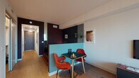 This single-floor residence showcases a thoughtfully designed interior that balances bold aesthetics with practical functionality. The open-plan layout connects a dining area, living room, and kitchen in a cohesive flow, with wood-effect flooring running throughout the main living spaces.

The dining area features a striking teal half-wall partition, vivid orange mid-century style chairs, and a compact dark dining table, creating a visually distinct zone within the open plan. Adjacent to this, the living room is anchored by a wall-mounted flat-screen television above a walnut media unit, complemented by a mustard sofa, teal area rug, and colorful artwork that adds personality throughout.

The kitchen is sleekly outfitted with floor-to-ceiling light wood cabinetry, white countertops, a stainless steel range cooker with gas hob, and an integrated microwave, offering a refined and fully functional cooking space.

Floor-to-ceiling glazing lines the living area, flooding the interior with natural light and providing expansive urban views. A dedicated study nook sits beside the glazing, making the most of the outlook.

The bathroom is finished in light stone-effect tiling, maintaining a clean and minimal aesthetic consistent with the rest of the residence.