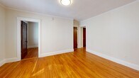 Located at 11 Shepley St in Portland, Maine, this two-bedroom, one-bathroom unit offers a thoughtfully arranged single-floor layout that maximizes every square foot. Warm hardwood flooring runs throughout the main living areas and bedrooms, lending a classic New England character to the space. The primary bedroom is generously proportioned relative to the overall footprint, featuring a large double-hung window with natural light, crisp white trim, and a traditional wood door. A ceiling fan is also present in one of the bedrooms, adding comfort. The kitchen is well-appointed with two-tone cabinetry — white upper cabinets and wood-toned lower drawers — complemented by a white subway tile backsplash, a stainless steel range with an overhead vent hood, and ample counter space. The bathroom is clean and modern, featuring a walk-in shower fully tiled in white subway tile with matte black fixtures and a frameless glass door. A hallway connects the rooms, contributing to an efficient flow throughout the unit. Crown molding and classic white baseboards add architectural detail, while neutral wall tones keep the interior feeling bright and open despite its compact size.
