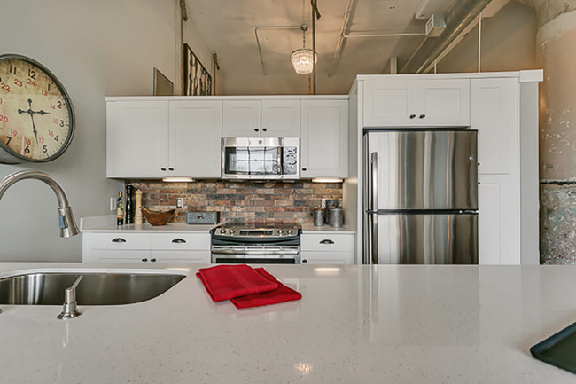 Moderna cocina con gabinetes blancos y placa para salpicaduras estilo ladrillos, con una encimera de cuarzo de color blanco - Lofts at Mockingbird Station Apartments