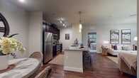 This single-floor residence offers a thoughtfully designed open-concept layout that seamlessly connects the kitchen, dining, and living areas. The kitchen is a functional centerpiece, featuring rich dark cabinetry, stainless steel appliances including a refrigerator, microwave, and range, and granite countertops that extend to a breakfast bar with bar stool seating. Elegant pendant lighting and a track light system illuminate the space with warm ambiance. Hardwood-style flooring flows throughout the main living areas, adding a polished, cohesive aesthetic.

The living room is bright and inviting, with natural light filtering through windows dressed in bold chevron-patterned curtains. A ceiling fan overhead and ample wall space make it both comfortable and versatile. A separate dining nook provides an intimate space for meals.

The primary bedroom is a serene retreat, highlighted by a striking reclaimed wood accent wall, plush carpeting, and a ceiling fan. Natural light enters through a well-positioned window. The second bedroom is equally comfortable, featuring hardwood-style flooring and natural light.

Both bathrooms maintain the design consistency of the home, offering dark cabinetry vanities with granite countertops, large mirrors, and tile flooring. One bathroom includes a shower-tub combination, while the other features a walk-in shower.