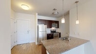 Located at 527 Old Bridge Turnpike in East Brunswick, NJ, this 2-bedroom, 1-bathroom residence offers a well-designed single-level layout that maximizes comfort and functionality. The open-concept kitchen and living area serves as the heart of the home, featuring rich dark-espresso cabinetry, granite countertops, a central island with a built-in sink, and a full suite of stainless steel appliances including a refrigerator, electric range, and microwave. Pendant lighting above the island adds a modern touch, while a classic white subway tile backsplash completes the kitchen aesthetic. Warm hardwood-style flooring flows throughout the main living areas, complemented by an abundance of natural light from large windows. The spacious primary bedroom is generously sized, offering plush carpeting and a bright window with exterior views. The second bedroom also features carpet flooring and a well-proportioned window. The full bathroom includes a soaking tub with a subway-tiled surround and brushed nickel fixtures. A dedicated closet provides additional storage. Clean white walls and a neutral palette throughout create a bright, move-in-ready environment with a modern, cohesive design sensibility.