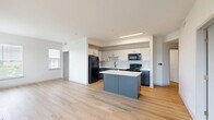 Located at 14883 Orchard Pkwy in Westminster, CO, this well-appointed 2-bedroom, 2-bathroom residence offers a thoughtfully designed single-level layout. The open-concept kitchen and living area serves as the heart of the home, featuring light wood-tone flooring throughout. The kitchen is outfitted with two-tone cabinetry — white upper cabinets paired with slate-gray lower cabinets — complemented by a white countertop island, a white subway tile backsplash, and black appliances including a refrigerator, range, and microwave. The living area is bright and airy, with large windows and a sliding glass door that opens to a private balcony overlooking a landscaped outdoor area. Both bedrooms are carpeted and receive natural light through sizable windows fitted with horizontal blinds, and each includes a ceiling fan. The bathrooms are finished with white cabinetry, white countertops, black hardware accents, and wood-tone flooring. A connecting hallway links the bedrooms and bathrooms, with five closets distributed throughout the residence for generous storage. The overall aesthetic is clean and contemporary, with a neutral color palette and modern finishes throughout.