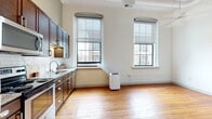 Located at 345 E Deshler Ave in Columbus, Ohio, this efficient one-bedroom, one-bathroom space offers a thoughtfully arranged single-floor layout. Warm-toned hardwood floors flow throughout, tying together the various rooms with a cohesive, inviting character.

The combined kitchen and living area serves as the heart of the space, bathed in natural light from two large arched windows that frame views of the surrounding neighborhood. The kitchen is well-appointed with rich dark-wood cabinetry, granite-style countertops, a classic white subway tile backsplash, and a full suite of stainless steel appliances including a refrigerator, range, microwave, and dishwasher.

The bedroom is a quiet, well-defined retreat featuring a ceiling fan and access to a closet, maintaining the same warm hardwood flooring found throughout. The bathroom is clean and modern, offering a tiled walk-in shower with sliding glass doors, a vanity with storage, and a toilet.

Additional practical features include a dedicated entrance, in-unit laundry, and two closets for ample storage. The overall ambiance is bright and functional, with white walls and natural wood floors creating a clean, neutral backdrop throughout the entire space.