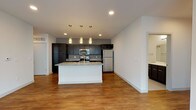 Located at 704 Williamson Street in Madison, Wisconsin, this single-floor unit offers a thoughtfully designed contemporary layout along one of the city's most well-known corridors. The open-concept kitchen and living area serves as the heart of the space, anchored by a central island with granite countertops and a crisp white base. Dark espresso cabinetry lines the kitchen walls, complemented by stainless steel appliances including a range, microwave, and refrigerator, while a trio of pendant lights adds focused illumination above the island. Warm hardwood-style flooring runs throughout the main living areas, contributing to a clean, cohesive aesthetic. An in-unit stacked washer and dryer is conveniently tucked within the unit. The living area benefits from generous natural light through large windows and provides access to a private balcony with outdoor views of the surrounding neighborhood. Bedrooms are carpeted for comfort and feature large windows that bring in additional daylight. Two bathrooms are finished with dark vanity cabinetry, solid-surface countertops, and clean tile or vinyl flooring — one featuring a walk-in shower and the other a full tub-shower combination. The overall ambiance is modern, neutral, and move-in ready.