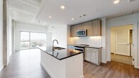 Located along Southwest Freeway in Houston, TX, this modern 2-bedroom, 2-bathroom residence offers a thoughtfully designed open-concept layout with contemporary finishes throughout. The living area is anchored by dramatic floor-to-ceiling windows that flood the space with natural light and frame sweeping city views, complemented by warm hardwood-style flooring and an exposed concrete ceiling detail that adds an industrial edge.

The kitchen is a standout feature, showcasing light wood cabinetry, a bold dark granite island with a double sink and bronze faucet, white subway tile backsplash, and a full suite of stainless steel appliances including a French door refrigerator and range. The open flow between the kitchen, dining, and living areas makes the layout feel expansive and functional.

Both bedrooms are generously proportioned with hardwood-style flooring, bright white walls, and ample natural light. The primary bedroom is particularly spacious and includes a walk-in closet with wire shelving. The bathrooms feature large-format tile flooring, wood-toned vanities with dark countertops, and a soaking tub. An in-unit laundry room with a full-size washer and dryer adds everyday convenience, rounding out this well-appointed urban residence.