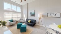 This single-floor unit is defined by its notably high ceilings, which lend an open, airy quality throughout the space. The living area benefits from dramatic floor-to-ceiling windows that flood the room with natural light, creating a bright and welcoming atmosphere. Light wood-tone flooring runs throughout, complementing the neutral gray wall palette. A ceiling fan adds both function and style to the living space.

The kitchen is well-equipped and thoughtfully designed, featuring crisp white shaker cabinetry extending to the upper reaches of the tall walls, granite countertops, a subway tile backsplash, and a full suite of stainless steel appliances including a refrigerator, range, microwave, and dishwasher. A kitchen island provides additional prep and gathering space.

The bedrooms are comfortably scaled, each with high ceilings, ceiling fans, and large windows that invite natural light. Light wood-tone flooring continues from the main living areas into the bedrooms. The bathroom includes a tub and shower combination with clean, neutral finishes. Overall, the space presents a cohesive modern aesthetic, with consistent materials and a calm, neutral color scheme throughout.