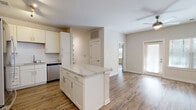 Located at 6104 Vintage Brunswick Circle in Brunswick, Georgia, this single-story, three-bedroom, two-bathroom home offers a well-designed layout with modern finishes throughout. Wood-look flooring flows consistently across the living areas, hallway, and bedrooms, giving the home a cohesive and contemporary feel.

The open-concept kitchen and living room serve as the heart of the home. The kitchen is outfitted with white shaker-style cabinetry, stainless steel appliances including a refrigerator, range, and microwave, a subway tile backsplash, and a central island topped with a marble-look countertop — ideal for both meal prep and casual dining. An arched architectural detail frames the transition between spaces, adding a subtle design touch.

The primary bedroom is a comfortable size, featuring a walk-in closet with wire shelving and its own en-suite bathroom. The en-suite includes a glass-enclosed walk-in shower, marble-look vanity countertop, white cabinetry, and tile flooring. Two additional bedrooms share a second full bathroom and each offer closet storage.

A dedicated laundry room comes equipped with a full-size washer and dryer and overhead wire shelving for added storage. The hallway connects all rooms efficiently, and natural light filters in through slatted blinds in the living and bedroom areas, creating a bright and welcoming atmosphere throughout.