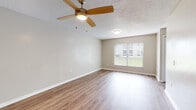 This single-story residence offers a practical and straightforward layout designed for comfortable everyday living. The living area serves as the heart of the home, featuring warm wood-look laminate flooring, neutral beige walls, and a ceiling fan with an integrated light fixture. A window fitted with vertical blinds allows natural light to filter into the space, creating a bright and open atmosphere.

The kitchen is well-appointed with white shaker-style cabinetry, granite-look countertops, a stainless steel sink, and black appliances including an electric range with overhead ventilation and a dishwasher. An adjacent window provides additional natural light while cooking.

A central hallway connects the main living spaces to the bedrooms and bathrooms. Both bedrooms are carpeted and finished in neutral tones, each featuring a window that brings in outside views and natural light. Louvered closet doors provide organized storage within the bedrooms.

The bathrooms each include a tub and shower combination with white tile surrounds and chrome fixtures, complemented by white vanities. Throughout the unit, textured ceilings and clean white baseboards contribute to a cohesive, neutral aesthetic.