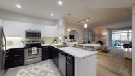 Located at 9800 Mira Lee Way in San Diego's Mira Mesa neighborhood, this single-floor residence showcases a thoughtfully designed open-concept layout with clean, contemporary finishes throughout. The kitchen is a standout feature, equipped with stainless steel appliances, a built-in microwave, a deep double sink, and a striking two-tone design pairing white upper cabinetry with dark lower cabinets against bright white quartz countertops. A peninsula with bar seating provides a seamless transition into the dining area, ideal for casual entertaining. Track and pendant lighting add warmth and definition to the space. The living room is generously proportioned, featuring plush carpeting, large windows that invite natural light, and sliding glass doors opening to an outdoor area with views of lush greenery. The bedroom offers a serene retreat with soft carpet, a ceiling fan, natural light from a window overlooking tropical foliage, and ample storage. The bathroom maintains the home's consistent aesthetic with dark cabinetry, a wide vanity mirror, and light wood-tone flooring. Throughout the residence, a neutral color palette, recessed lighting, and modern fixtures create a cohesive, polished ambiance suited for contemporary living in San Diego.