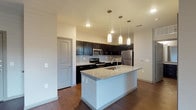 This single-floor 1-bedroom, 1-bathroom residence offers a thoughtfully designed layout with contemporary finishes throughout. The kitchen serves as a standout feature, showcasing rich dark cabinetry that extends to the ceiling, granite countertops, a tiled backsplash, and a full suite of stainless steel appliances including a range, microwave, and refrigerator. A central island with an integrated sink and matching granite surface provides additional prep space and casual seating, illuminated by elegant pendant lighting overhead. The open-concept design connects the kitchen seamlessly to the living area, which features rich wood-style flooring, a ceiling fan with light fixture, and French doors that invite natural light and provide outdoor access. Neutral wall tones and recessed lighting contribute to a clean, modern aesthetic throughout the common areas. The bathroom is well-equipped with a granite-topped double vanity paired with dark cabinetry, a tiled tub-surround combination, and wood-style flooring that ties the space together cohesively. Ample storage is provided through multiple closet doors visible throughout the unit. The overall design balances functionality and style, making for a comfortable and visually cohesive living environment.