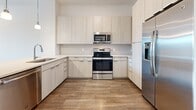 Located at 300 Central Ave in the heart of Sarasota, Florida, this contemporary single-floor residence offers a clean, modern aesthetic throughout. The open-concept kitchen serves as a central highlight, featuring light wood-toned cabinetry, a classic subway tile backsplash, a kitchen island with a stainless steel sink and pendant lighting above, and a full suite of stainless steel appliances including a refrigerator, range, microwave, and dishwasher. The kitchen flows seamlessly into the living area, which is finished with warm wood-look hardwood flooring and recessed lighting, creating a bright and welcoming atmosphere. Natural light filters in through windows with outdoor views, enhancing the open feel of the living space. The bedroom areas feature plush carpeting and generous windows with views to the outdoors, providing a comfortable and serene retreat. The bathroom is well-appointed with a wide vanity, light wood cabinetry, a large mirror, tile flooring, and a glass-enclosed shower with white subway tile surround. A dedicated in-unit laundry closet with a stacked washer and dryer adds everyday convenience. Throughout, the residence maintains a cohesive, neutral palette that is both modern and inviting.
