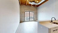 Located at 470 Market Ave SW in the heart of Grand Rapids, MI, this 2-bedroom, 2-bathroom loft offers a compelling blend of industrial character and modern finishes. The open-concept living and kitchen area is a standout, showcasing soaring ceilings with exposed wooden beams and visible ductwork that highlight the space's loft heritage. The kitchen features a peninsula with bar seating, grey flat-panel cabinetry, a subway tile backsplash, and stainless steel appliances, flowing seamlessly into the living area with light wood-tone luxury vinyl flooring throughout. The spacious primary bedroom features dramatic angled ceilings with a skylight that draws in natural light, adding architectural interest and an airy feel. The second bedroom is well-proportioned with high ceilings and exposed ductwork consistent with the loft aesthetic. Both bathrooms are finished with crisp white subway tile laid in a herringbone pattern, dark grey floor tile, and matte black fixtures — one featuring a walk-in glass shower and the other a soaking tub/shower combo. A connecting hallway provides functional flow between the bedrooms and bathrooms. The overall ambiance is modern-industrial, clean, and cohesive, making this a distinctive urban living option in downtown Grand Rapids.