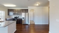 This single-floor residence offers a thoughtfully designed open-concept layout finished with a cohesive neutral palette throughout. The living area features crown molding, a ceiling fan, and multiple windows that invite natural light, with hardwood flooring transitioning seamlessly into carpeted spaces. Pendant lighting illuminates the dining area, which connects directly to the kitchen via a granite-topped breakfast bar with an undermount sink. A glass door provides access to the outdoors from the dining space.

The kitchen is well-equipped with dark espresso cabinetry, granite countertops, a tile backsplash, and a full suite of stainless steel appliances including a French door refrigerator, electric range, and built-in microwave. An elegant arched passageway connects the kitchen to the remainder of the home.

Bedrooms are carpeted and include ceiling fans and windows with exterior views. Each features walk-in closet space with wire shelving systems. Two full bathrooms mirror each other in design, each offering dark vanity cabinetry, granite countertops, tile flooring, and a tub-shower combination. A dedicated laundry room accommodates a full-size washer and dryer with additional wire shelving above.