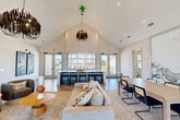 Located at 180 Hughes Rd in Madison, Alabama, this single-floor community clubhouse offers a thoughtfully designed gathering space that blends modern aesthetics with welcoming comfort. The centerpiece is a dramatic open-plan living area anchored by soaring vaulted ceilings clad in white shiplap, adorned with striking sculptural chandeliers that create an immediate visual impact. Herringbone-patterned hardwood flooring runs throughout, lending an elegant continuity to the space.

The main living area is generously proportioned, featuring a plush seating arrangement, curated artwork, and a large bar counter with sleek black barstools positioned beneath expansive windows that flood the interior with natural light and offer open views of the surrounding neighborhood. Adjacent dining areas provide multiple seating configurations, including an intimate round-table nook with bold dark accent walls and a brighter banquette-style dining space lined with floor-to-ceiling windows.

A separate lounge area near the hallways offers a relaxed setting with modern accent chairs, built-in display shelving, and a mounted flat-screen display — ideal for a leasing or reception function. Throughout the space, carefully selected wall art, layered rugs, and warm-toned furnishings contribute to a cohesive, contemporary atmosphere that is both functional and visually refined.
