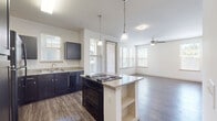 This single-story residence offers a thoughtfully designed open-concept layout that seamlessly connects the kitchen and living areas, creating a spacious and functional flow throughout. The kitchen serves as a central focal point, showcasing dark espresso cabinetry, granite countertops, and a large center island equipped with a cooktop and built-in shelving beneath. Pendant lighting hangs above the island, complementing the suite of black appliances that includes a refrigerator, range, dishwasher, and microwave. Hardwood-style flooring extends throughout the entire unit, providing a cohesive and durable finish.

The open living area benefits from an abundance of natural light, delivered through multiple windows dressed with horizontal blinds, and is finished with a ceiling fan overhead. A dedicated dining or flex space adjacent to the living room features a tray ceiling detail and additional windows that further enhance the brightness of the interior.

The bedrooms are generously proportioned, each featuring ceiling fans, ample natural light, and neutral walls. The bathrooms are well-appointed with granite-topped dark vanities, large mirrors, and hardwood-style flooring. One bathroom includes a walk-in closet, while another offers a full tub-shower combination. The unit presents a clean, modern aesthetic throughout.