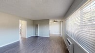 Located at 12401 Studebaker Rd in Norwalk, California, this single-story unit offers two bedrooms and one bathroom within a well-organized floor plan. Throughout the living areas, dark wood-style laminate flooring provides a cohesive and easy-to-maintain surface, complemented by neutral gray walls and white baseboards that create a clean, contemporary aesthetic. Textured ceilings are present throughout the unit.

The living area is generously proportioned, featuring a wall-mounted air conditioning unit, horizontal blinds, and a sliding glass door that allows natural light to filter in. A second connected living space is equipped with a ceiling fan, extending the functional area of the home. The front entry door features a decorative fanlight window, adding a welcoming touch.

The kitchen is a standout feature, showcasing two-tone cabinetry with white upper cabinets and slate-blue lower cabinets, white quartz countertops, a stainless steel sink, and stainless steel appliances including a gas range and microwave. A recessed skylight panel provides bright overhead illumination.

Each bedroom includes a ceiling fan with a light fixture and dark wood-style flooring. One bedroom features a set of sliding double closet doors, offering practical storage. The bathroom is outfitted with a tub-shower combination, a window for natural light and ventilation, and a vanity with modern cabinetry.