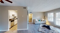 This single-floor residence offers a functional and comfortable layout designed to maximize everyday living. The open living area is bright and welcoming, featuring light-toned hardwood-style flooring, neutral gray walls, and a textured ceiling. A set of white-framed patio doors floods the space with natural light while providing direct outdoor access. The galley-style kitchen is thoughtfully designed with white cabinetry, dark granite-style countertops, a stainless steel sink, and stainless steel appliances including an electric range and built-in microwave — all set over light hardwood-style flooring that ties the common areas together seamlessly. Two bedrooms offer a calm retreat, each featuring plush wall-to-wall carpeting, soft neutral tones, and windows fitted with horizontal blinds that allow for adjustable natural light. The full bathroom is well-equipped with a combined tub and shower, a white vanity topped with a dark countertop, a large mirror with overhead lighting, and ample storage drawers. Throughout the residence, consistent use of neutral tones and clean finishes creates a cohesive, move-in-ready atmosphere suited for comfortable daily living.