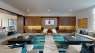 Located at 2508 April Liu Ln. in Charlotte, NC, this contemporary single-floor community clubhouse offers a thoughtfully designed, open layout with a cohesive modern aesthetic. The space is anchored by expansive lounge areas furnished with large sectional sofas, bold teal and gold-striped area rugs, and neutral tones that create a welcoming yet upscale atmosphere. Large floor-to-ceiling windows and glass doors flood the interiors with natural light while providing views of the surrounding outdoor areas.

A dedicated lounge zone features a warm wood-paneled accent wall with illuminated built-in shelving and a mounted display screen, flanked by stylish accent chairs — ideal for relaxed gatherings. The game room area includes a billiards table beneath a striking multi-pendant chandelier, with bar-height seating and curated wall art adding personality and energy to the space.

The wet bar area is a standout feature, boasting a sleek white quartz countertop, metallic mosaic tile backsplash, warm wood panel accents, and three bold matte-black pendant lights overhead, creating a refined entertaining hub. Rich hardwood flooring flows throughout much of the space, complementing the clean white walls and recessed lighting. Together, these elements create a sophisticated and inviting environment well-suited for socializing and community engagement.