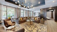 Located at 200 E Six Forks Rd in Raleigh, NC, the Anderson Flats amenity and leasing space is a thoughtfully designed single-floor community hub spanning a generously sized footprint. The entrance lobby immediately commands attention with a dramatic curved dark-wood feature wall bearing the Anderson Flats branding, flanked by slatted architectural columns and complemented by contemporary lounge seating arranged over a textured area rug.

Beyond the lobby, a spacious social lounge features a striking tray ceiling with bold dark accents, floor-to-ceiling windows that flood the space with natural light, and lush greenery views. An eye-catching sculptural chandelier with globe bulbs anchors the seating area, which includes large sectional sofas and organic wood accent tables. A full-size billiards table with pendant lighting serves as the centerpiece of the game area, complete with a wet bar and cabinetry nearby.

A well-appointed coffee bar showcases rich wood cabinetry, quartz countertops, and a bold chevron tile backsplash. Private meeting rooms accessible via sliding barn doors offer functional workspace options. The space connects seamlessly to an outdoor terrace through expansive glass sliding doors, where bar-height seating and greenery create an inviting al fresco setting.