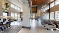 Located at 355 Eldorado Blvd in Broomfield, Colorado, this contemporary coworking space delivers a polished and professional environment designed for productivity and collaboration. The single-floor layout offers a generous footprint that flows seamlessly from one functional zone to the next.

The entrance lobby sets an immediate tone of sophistication, featuring soaring ceilings with warm wood accents, large-format tile flooring, a striking sculptural chandelier, and glass-paneled staircase railings. An eye-catching ornamental light installation adds an artistic focal point near the entry.

The main coworking area is bathed in natural light from expansive floor-to-ceiling windows along multiple walls, offering sweeping outdoor views of the surrounding Broomfield landscape. High ceilings with pendant lighting in brushed brass and copper tones create an elevated atmosphere. Flexible seating arrangements include modern lounge chairs, modular sofas, and open desk stations suited to a variety of work styles.

A dedicated media lounge features built-in warm wood cabinetry, wall-mounted displays, and swivel chairs arranged for presentations or group viewing. A well-appointed refreshment station with a coffee system, microwave, and under-counter refrigeration supports daily convenience. Textured patterned carpet, tasteful artwork, and curated greenery complete the refined, welcoming ambiance throughout this thoughtfully designed workspace.