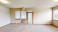 Located at 2636–2672 N Washington St in Cheney, WA, this one-bedroom, one-bathroom unit offers a well-organized single-floor layout designed for comfortable everyday living. The open-concept kitchen and living area serves as the heart of the unit, with the kitchen featuring warm wood cabinetry, laminate countertops, a full suite of white appliances including a coil-top electric range, built-in microwave, refrigerator, and dishwasher, all set atop durable hardwood-style flooring. A window above the kitchen sink brings in natural light and exterior views. The living area transitions seamlessly from the kitchen, offering plush neutral carpeting, a wall-unit air conditioner, baseboard heating, and a private exterior door flanked by multiple windows that fill the space with ample daylight. The bedroom is a comfortable, well-proportioned room with a large bank of windows overlooking the surrounding neighborhood, plush carpeting, and access to a dedicated closet. A second closet is conveniently located near the kitchen area. The full bathroom includes a tub/shower combo with built-in shelving and hardwood-style flooring. Warm beige and yellow accent tones throughout create a welcoming, cohesive ambiance across the entire unit.