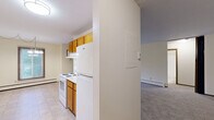 Located at 2653 Rice Creek Rd in New Brighton, MN, this 2-bedroom, 1-bathroom unit offers a practical and comfortable single-floor layout. The galley-style kitchen is efficiently designed with warm oak cabinetry lining both walls, white appliances including an electric range and refrigerator, a stainless steel sink, light countertops, and tile flooring — providing ample storage and workspace. The kitchen opens toward the main living area, which is carpeted and bathed in natural light from a sliding glass door that leads to a private balcony. A wall-mounted air conditioning unit serves the living space, and a baseboard heating system runs throughout the home. Both bedrooms are carpeted and feature neutral cream-toned walls. The primary bedroom includes a large sliding-door closet with rich wood-paneled doors, offering generous storage. A second closet provides additional organization. The full bathroom is finished with white tile flooring, a tub-shower combination with tile surround, a toilet, and a vanity with a granite-patterned countertop. Textured ceilings are consistent throughout the unit. The overall ambiance is clean, neutral, and functional, making it a comfortable and move-in ready home.