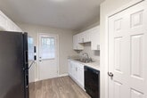 Located at 1940 Atlanta Rd SE in Smyrna, Georgia, this one-bedroom, one-bathroom residence offers a functional and well-appointed single-floor layout. The living area features wood-look laminate flooring and a neutral gray color palette, creating a clean, modern atmosphere. A distinctive pass-through window connects the living room to the kitchen, allowing natural light and an open sightline between the two spaces. The kitchen is equipped with white shaker-style cabinetry, granite-look countertops, a stainless steel sink, a black dishwasher, and a full-size black refrigerator. A door in the kitchen provides direct exterior access, with a window that brings in additional natural light. The spacious bedroom is finished with plush carpeting and includes a walk-in closet, offering ample storage. A wall-mounted mini-split HVAC unit provides efficient climate control in the bedroom. The full bathroom features white subway tile surrounding a tub and shower combo, with a small frosted window for ventilation and privacy. Throughout the residence, white trim and neutral tones contribute to a cohesive, move-in-ready aesthetic. The overall layout makes efficient use of its footprint, offering comfort and practicality in a well-maintained setting.