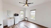 Located at 732 E Santa Clara St in Ventura, California, this efficiently designed single-room unit offers a clean, functional layout ideal for comfortable solo living. The main living area features durable wood-look flooring throughout, crisp white walls, and clean white baseboard trim that lend a bright, modern feel to the space.

Two double-hung windows allow generous natural light to pour in, framing views of the surrounding Ventura neighborhood and local greenery, including glimpses of palm trees. A modern ceiling fan with a brushed gold-and-silver finish provides both overhead lighting and air circulation.

The kitchenette area is neatly integrated along one wall, equipped with a compact white refrigerator, microwave, a two-burner cooktop, and a small sink with white cabinetry beneath — offering essential cooking and food storage amenities. A wall-mounted heater ensures year-round comfort.

Two interior doors lead to a dedicated closet and a secondary room or entry, both featuring clean white finishes and modern matte black hardware that complement the overall aesthetic. The uncluttered wall space throughout provides flexibility for personal furnishing arrangements.

This unit combines practical amenities with a clean, contemporary finish in a convenient Ventura location.