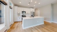 Located at 795 Ironwood Flats Cir in Brandon, FL, this single-story home showcases a clean, modern design with a cohesive neutral palette throughout. The open-concept living area is anchored by light wood flooring that reflects natural light pouring in through large windows and glass-paneled French doors, which open to an outdoor area and create a seamless indoor-outdoor connection.

The kitchen is a standout feature, equipped with white shaker cabinetry, a subway tile backsplash, stainless steel appliances including a range, over-the-range microwave, and refrigerator, plus a generous center island with a white quartz countertop, sink, and recessed lighting above. Matte black hardware adds a contemporary touch throughout.

The bedrooms are carpeted for comfort and feature ceiling fans and dual windows that invite plenty of natural light and outdoor views. The primary suite includes a well-appointed en-suite bathroom with a dual-sink vanity, white cabinetry with black hardware, light wood flooring, a glass-enclosed shower, and direct access to a spacious walk-in closet outfitted with multi-level wire shelving. A secondary bathroom mirrors the same refined aesthetic with matching finishes, a single vanity, and a shower-tub combination.