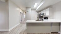 This single-floor unit offers a bright, contemporary design characterized by a consistent neutral color palette, light-toned luxury vinyl plank flooring throughout the main living areas, and plush carpeting in the bedrooms. The open-concept kitchen serves as a functional centerpiece, featuring white upper cabinetry, sage-toned lower cabinets, white quartz countertops, a peninsula with an integrated sink, and a full suite of stainless steel appliances including a refrigerator, electric range, microwave, and dishwasher. A skylight above the kitchen enhances the sense of brightness in the space. The living area is generously proportioned, offering ample room for furniture arrangement, and includes a large window fitted with vertical blinds that allows natural light to flow in. Two full bathrooms are finished with wood-look vinyl flooring, white quartz vanity tops, sage cabinetry with brushed hardware, and tub-shower combinations. The bedrooms feature soft carpeting and windows with horizontal blinds. One bedroom includes a spacious walk-in closet equipped with multi-level hanging rods. The entry area provides two access doors, adding practical functionality to the layout.
